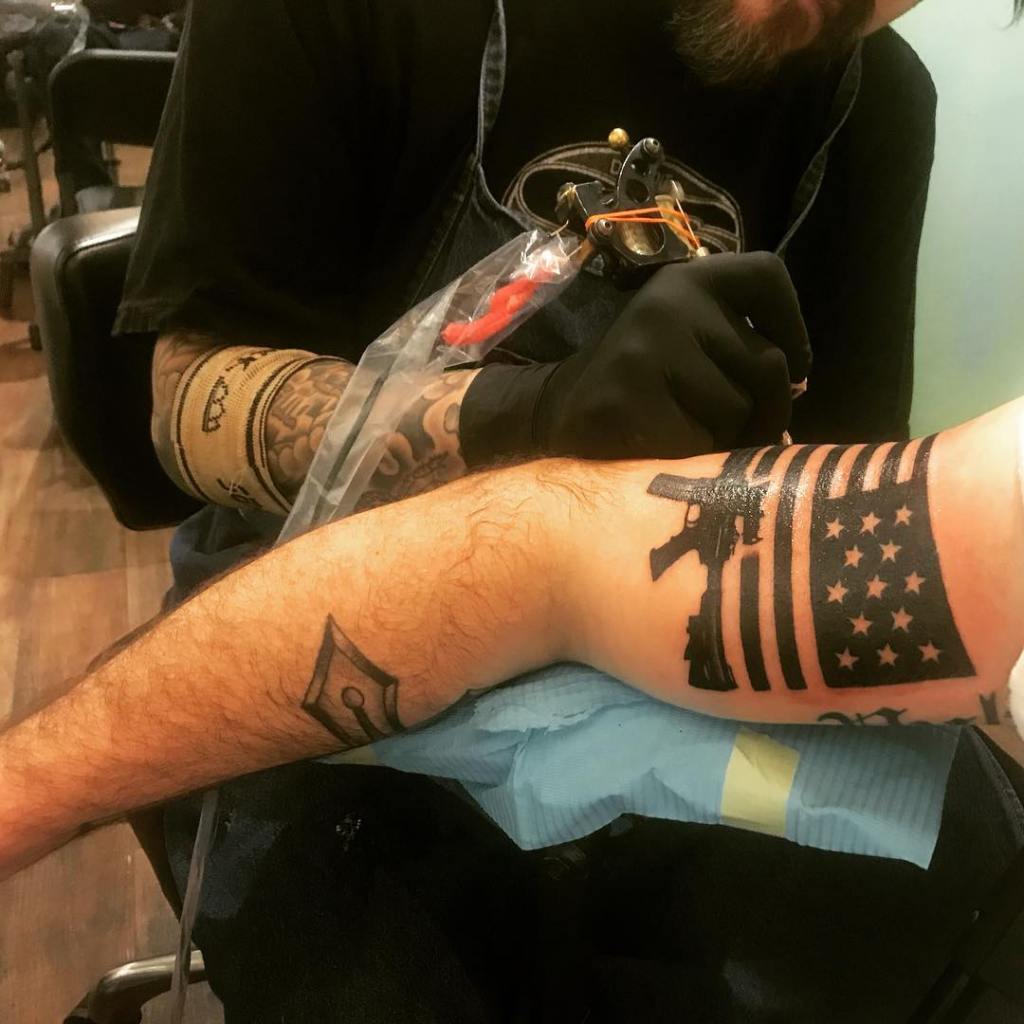 Hegseth's upper arm features an American flag with an AR-15 underneath it.