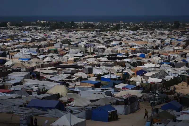 Displaced Palestinians walk through a tent camp in Muwasi, an area that Israel has designated as a safe zone, in Khan Younis southern Gaza Strip